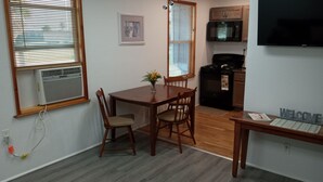 Un coin repas avec une table et des chaises en bois, un petit vase avec des fleurs, et un espace cuisine équipé d’un four à micro-ondes et d’une cuisinière.