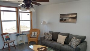 Un salon avec un canapé gris, une table basse en bois, un fauteuil en osier et un lampadaire.