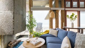 A modern living room with a blue sofa, a round wooden coffee table, and a large stone pillar. - Luxe Oceanfront w/ HotTub | Icon of Mission Beach (San Diego)