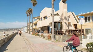 A coastal hotel with a modern design, featuring a beachside location, a bike rental service, and a sign indicating nearby amenities. - Luxe Oceanfront w/ HotTub | Icon of Mission Beach (San Diego)