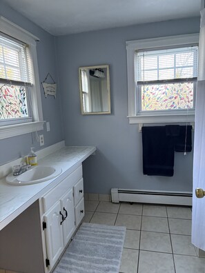 Een badkamer met een wit wastafelmeubel, een spiegel, een handdoekhouder en een raam met een glas-in-lood ontwerp.