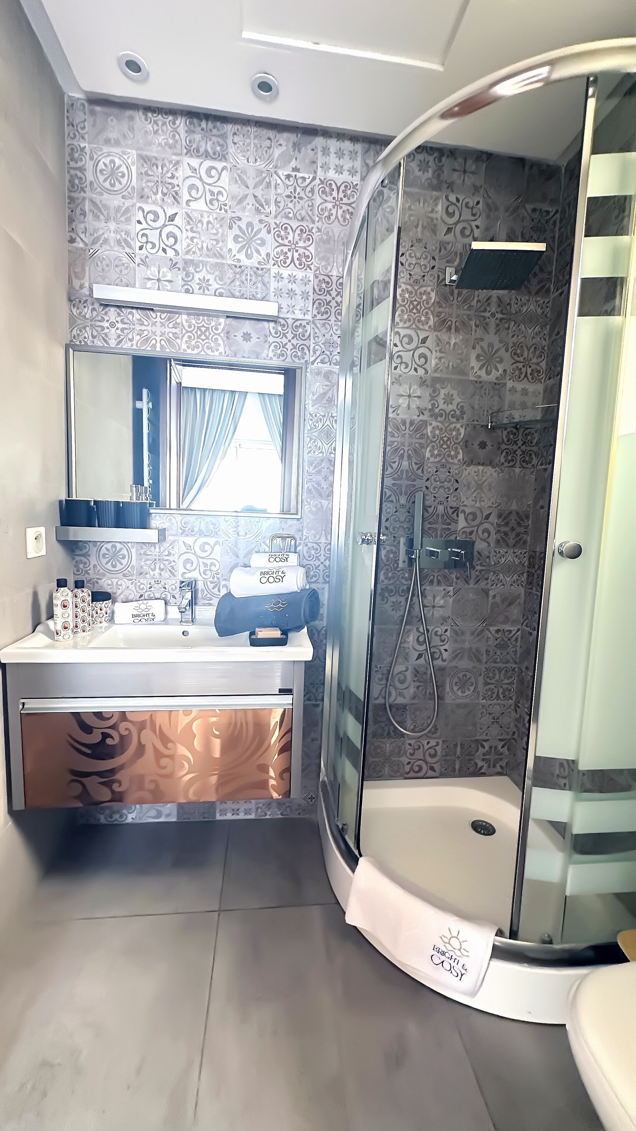 Une salle de bain moderne avec une douche à parois de verre, un meuble-lavabo avec un miroir et des carreaux décoratifs sur les murs.