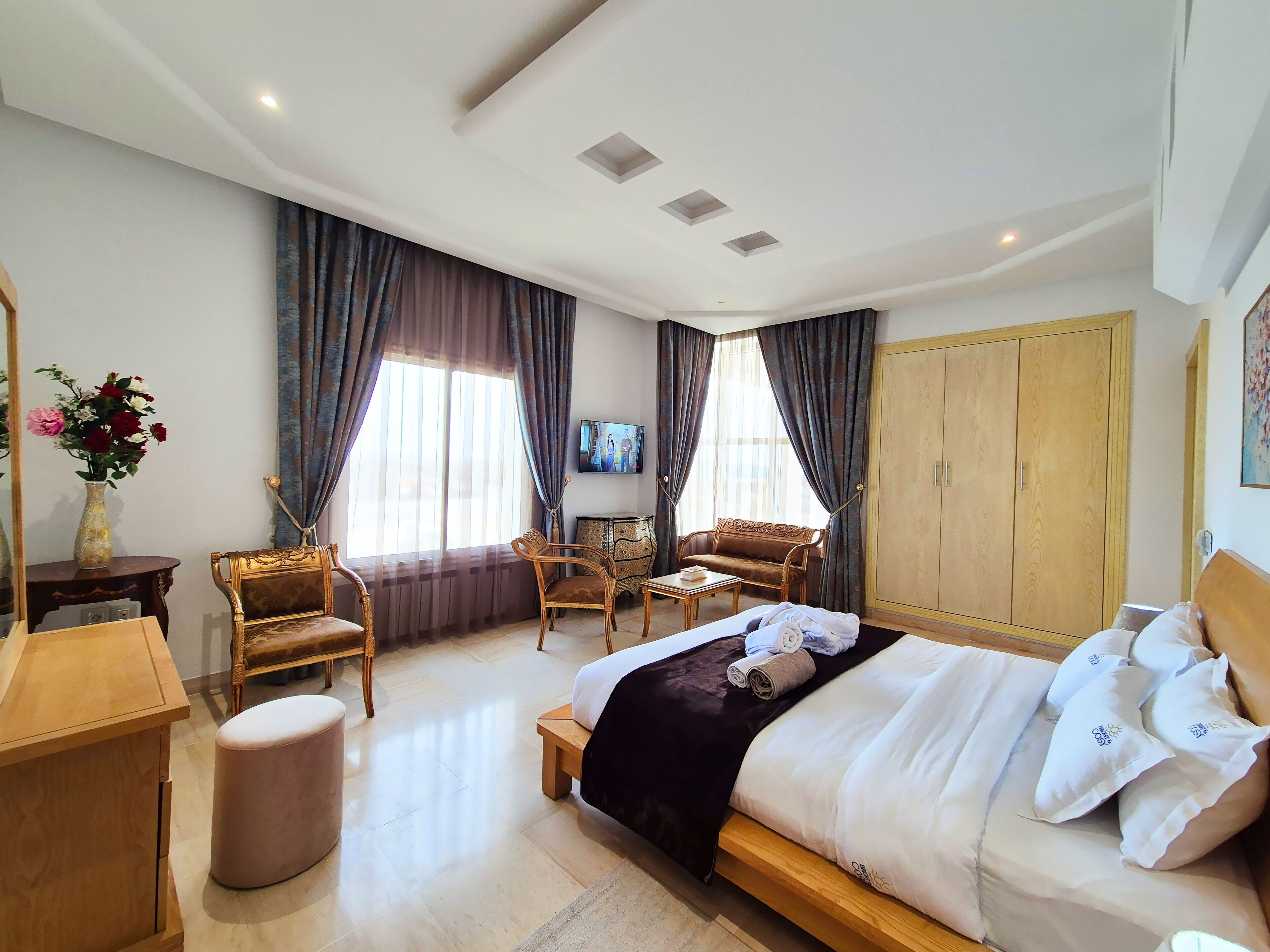 A hotel room with a large bed, two armchairs, a wooden cabinet, a small table, and a wardrobe.