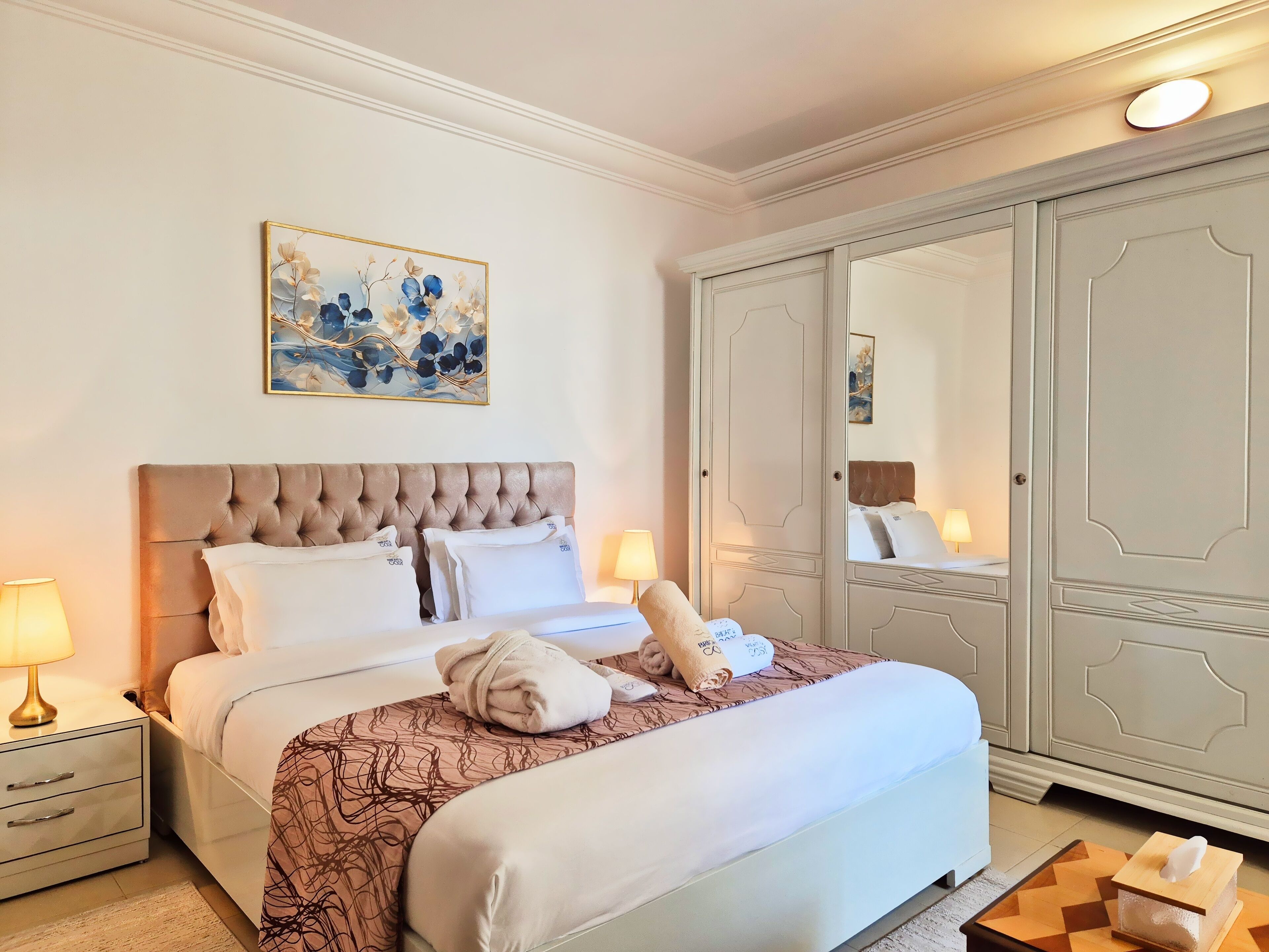 A neatly made bed with a patterned bedspread, a tufted headboard, and two bedside lamps.