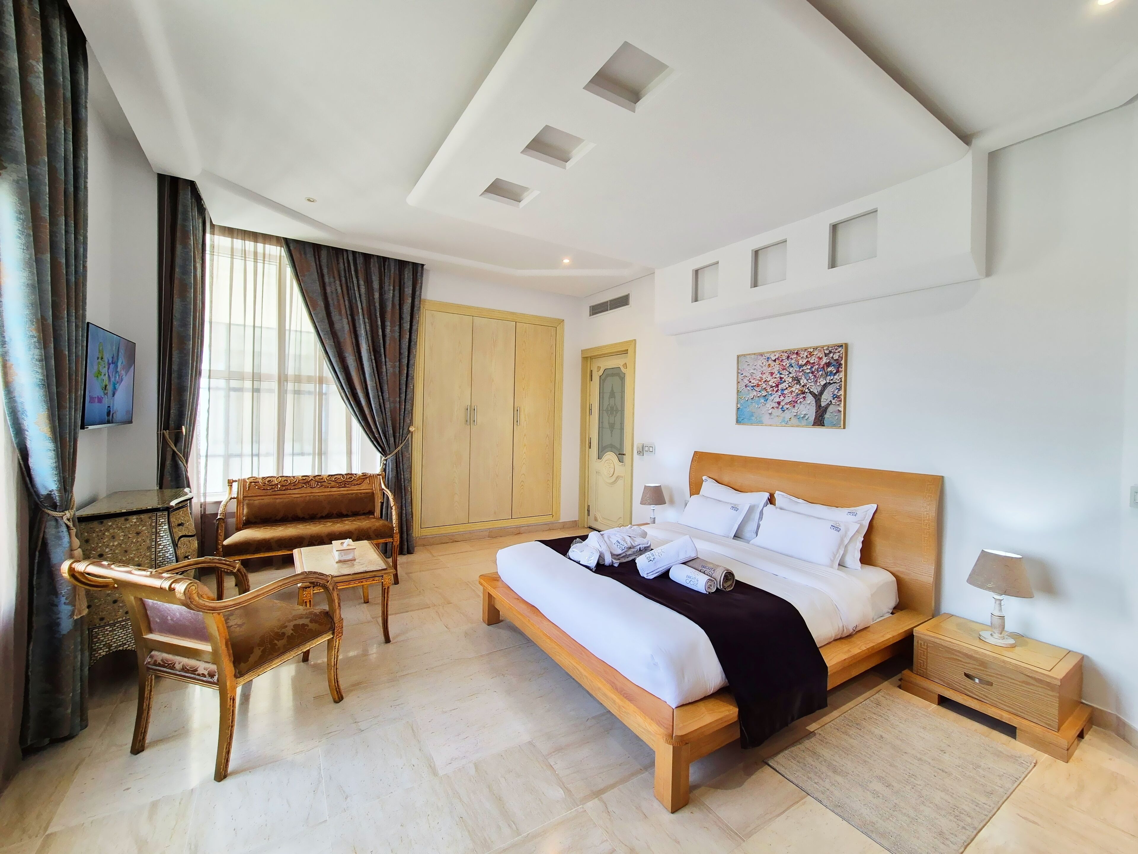 Una habitación de hotel con cama, mesita de noche de madera, sofá, sillón, armario y televisor.