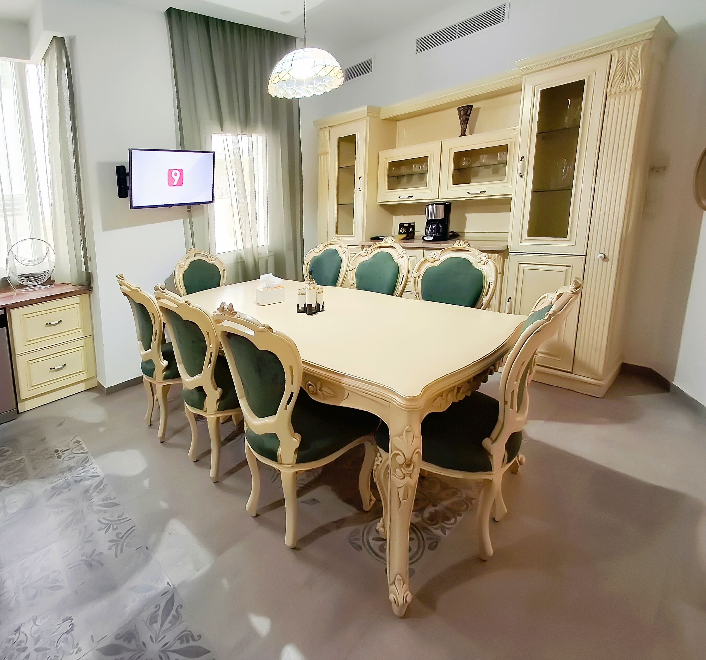 A dining area with a large table, ornate chairs, a television, and a cabinet with glass doors.