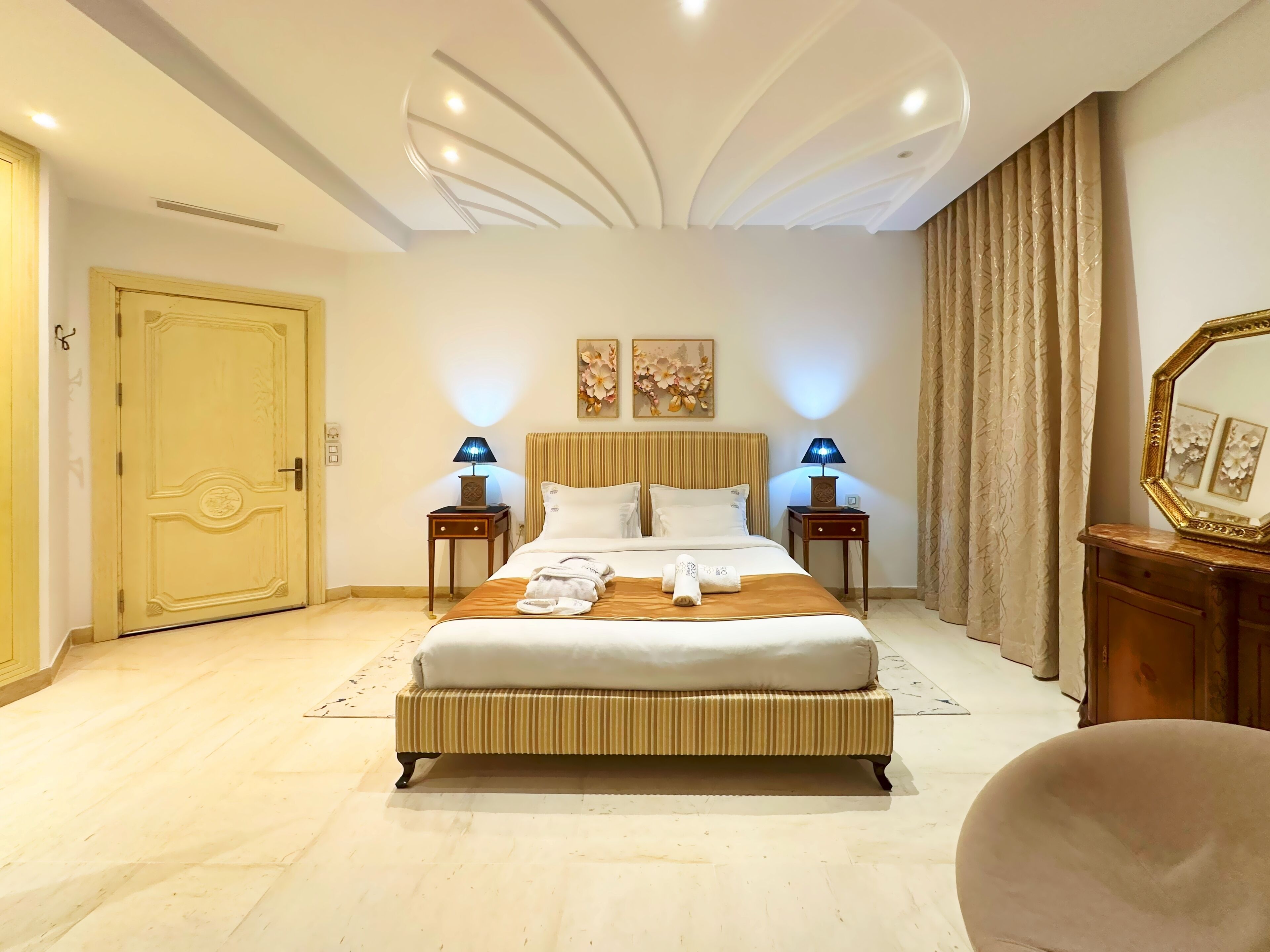 A spacious hotel room with a large bed, two bedside tables with lamps, a wooden headboard, and a large mirror.