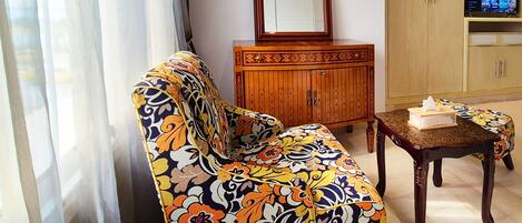 Una sala de estar con un sofá floral, un mueble de madera, una mesita con una caja de pañuelos y un televisor sobre un soporte de madera.
