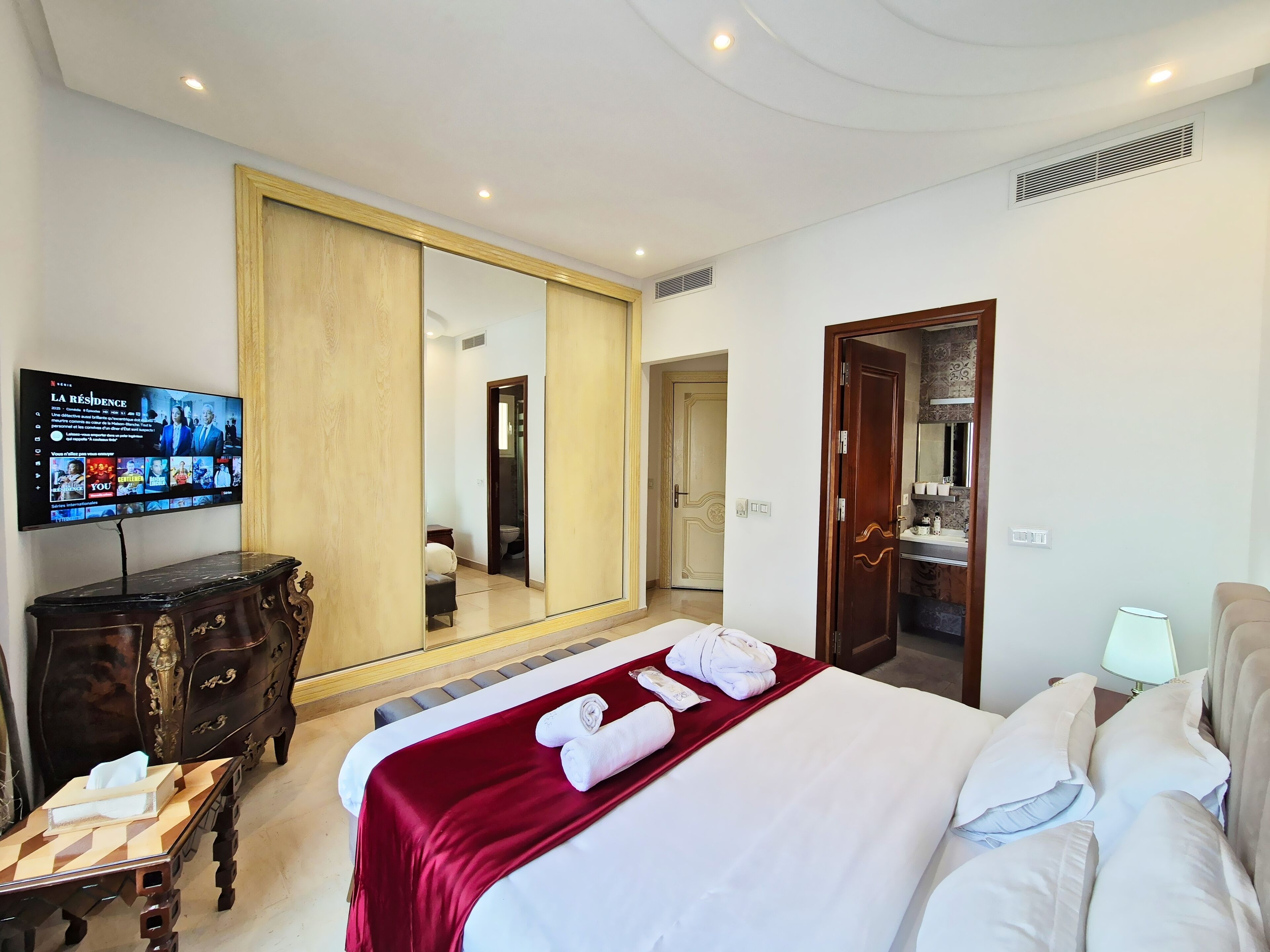 A hotel room with a large bed, a TV mounted on the wall, a wooden dresser, and a mirror.
