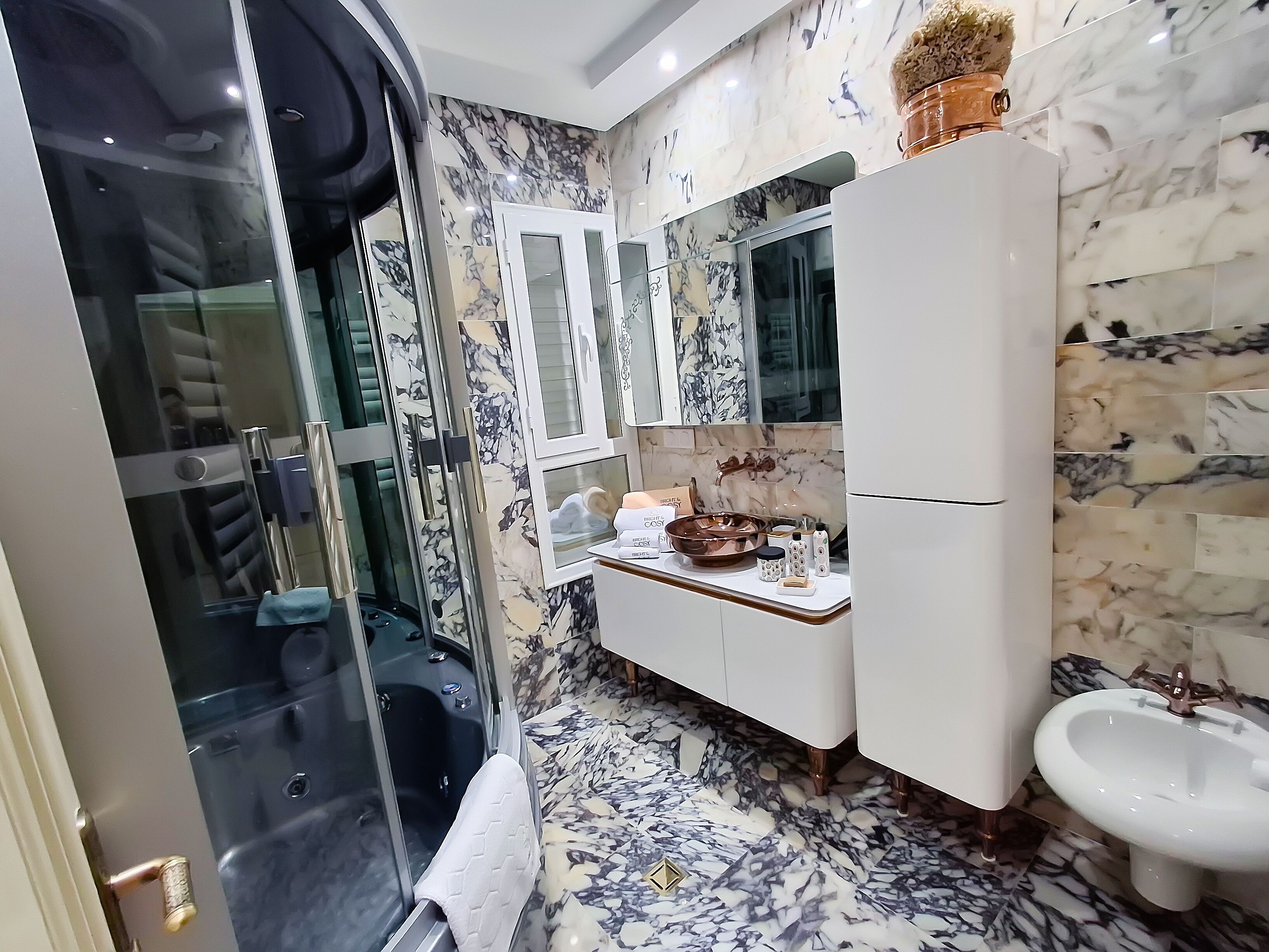 Un baño con ducha envuelta en vidrio, un tocador blanco con salpicadero de mármol y un lavabo blanco.