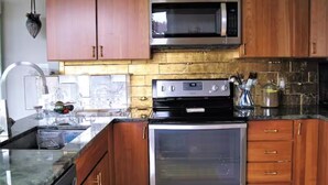 A kitchen with wooden cabinets, a stainless steel microwave, a built-in oven, and a granite countertop. - Apartment with Expansive Views;  River & Mountains Walk to Train, Main St, DIA (Beacon)
