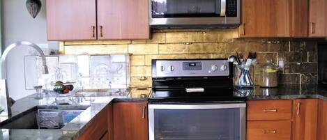 Uma cozinha com armários de madeira, micro-ondas de aço inoxidável, forno embutido e bancada de granito.