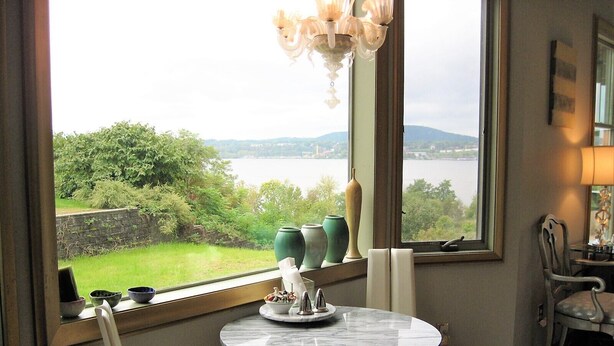 A room with a round marble table, a chair, a view of a lake, and a chandelier. - Apartment with Expansive Views;  River & Mountains Walk to Train, Main St, DIA (Beacon)