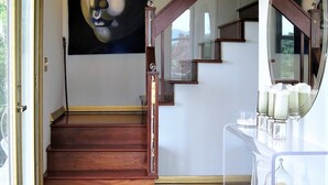 A staircase with wooden steps and a glass railing, a large abstract painting on the wall, and a modern light fixture above. - Apartment with Expansive Views;  River & Mountains Walk to Train, Main St, DIA (Beacon)