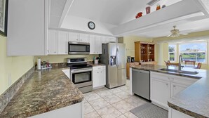 Una cucina moderna con mobili bianchi, ripiani in granito, un frigorifero in acciaio inossidabile e un forno integrato.