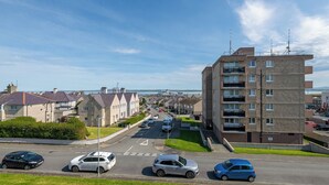 A residential street with houses, a multi-story building, and parked cars. - 3BDR Home in Central Holyhead (Holyhead)