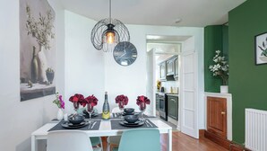 A dining area with a white table set for four, a black clock, and a green wall. - 3BDR Home in Central Holyhead (Holyhead)