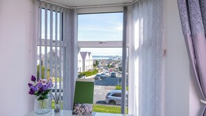 A room with a view of a street, a glass table with a vase of flowers, and a framed picture. - 3BDR Home in Central Holyhead (Holyhead)