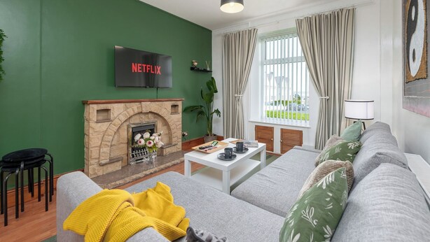 A living room with a fireplace, a sofa, a coffee table, and a TV mounted on the wall. - 3BDR Home in Central Holyhead (Holyhead)