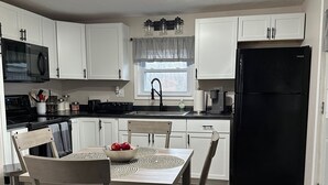 A modern kitchen with white cabinets, a black refrigerator, and a dining area with wooden chairs and a table. - Cozy 2-bedroom cabin with WiFi, AC in tranquil Moravia (Moravia)