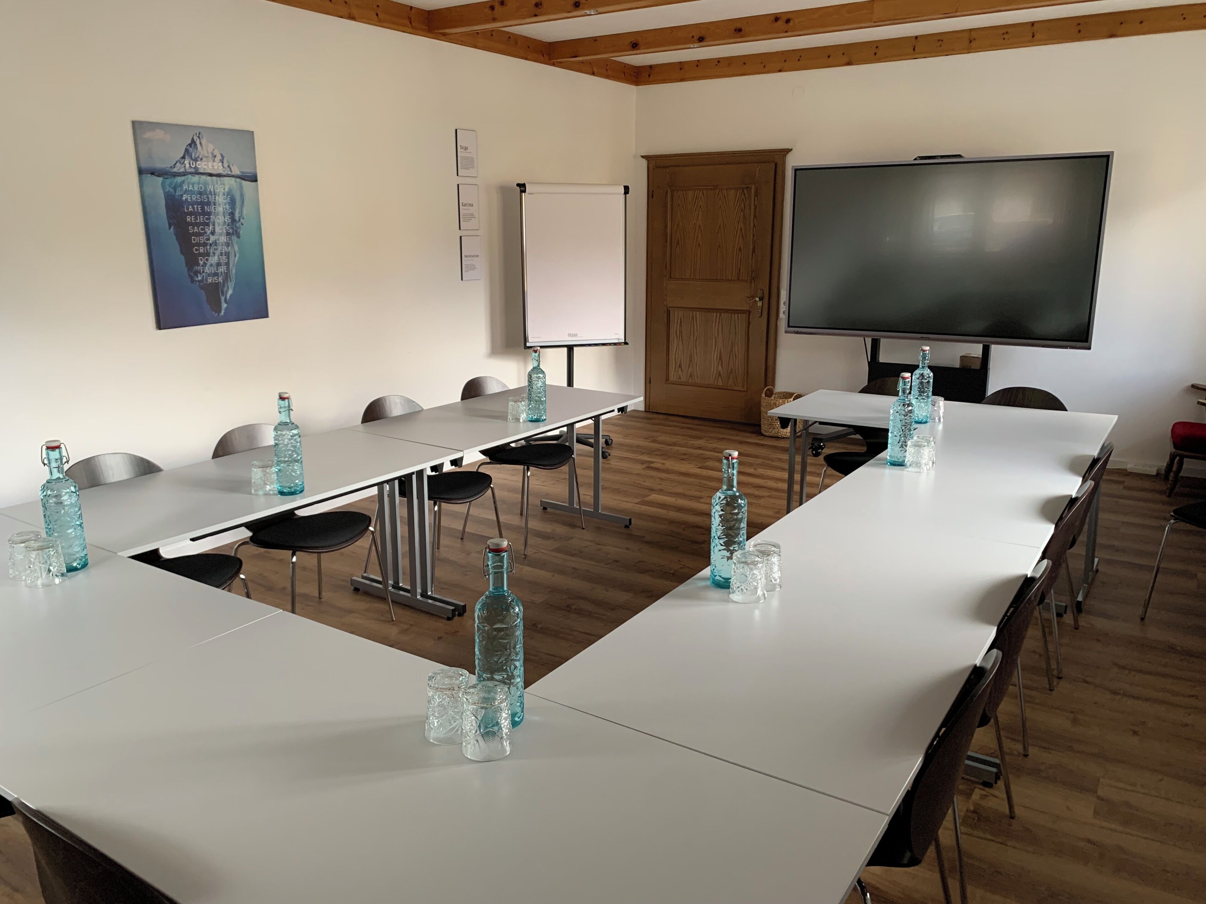 Une salle de conférence équipée de longues tables, de chaises, d’un tableau blanc, d’un écran de projection et d’une affiche motivante accrochée au mur.