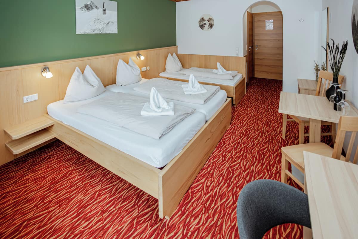 Habitación de hotel con dos camas, cabecera de madera, alfombra roja estampada, una mesa de comedor y una pequeña zona de estar.
