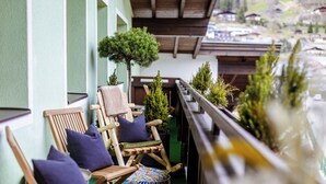 Un balcon avec des chaises et des coussins en bois, un petit arbre et une balustrade agrémentée de plantes en pot.