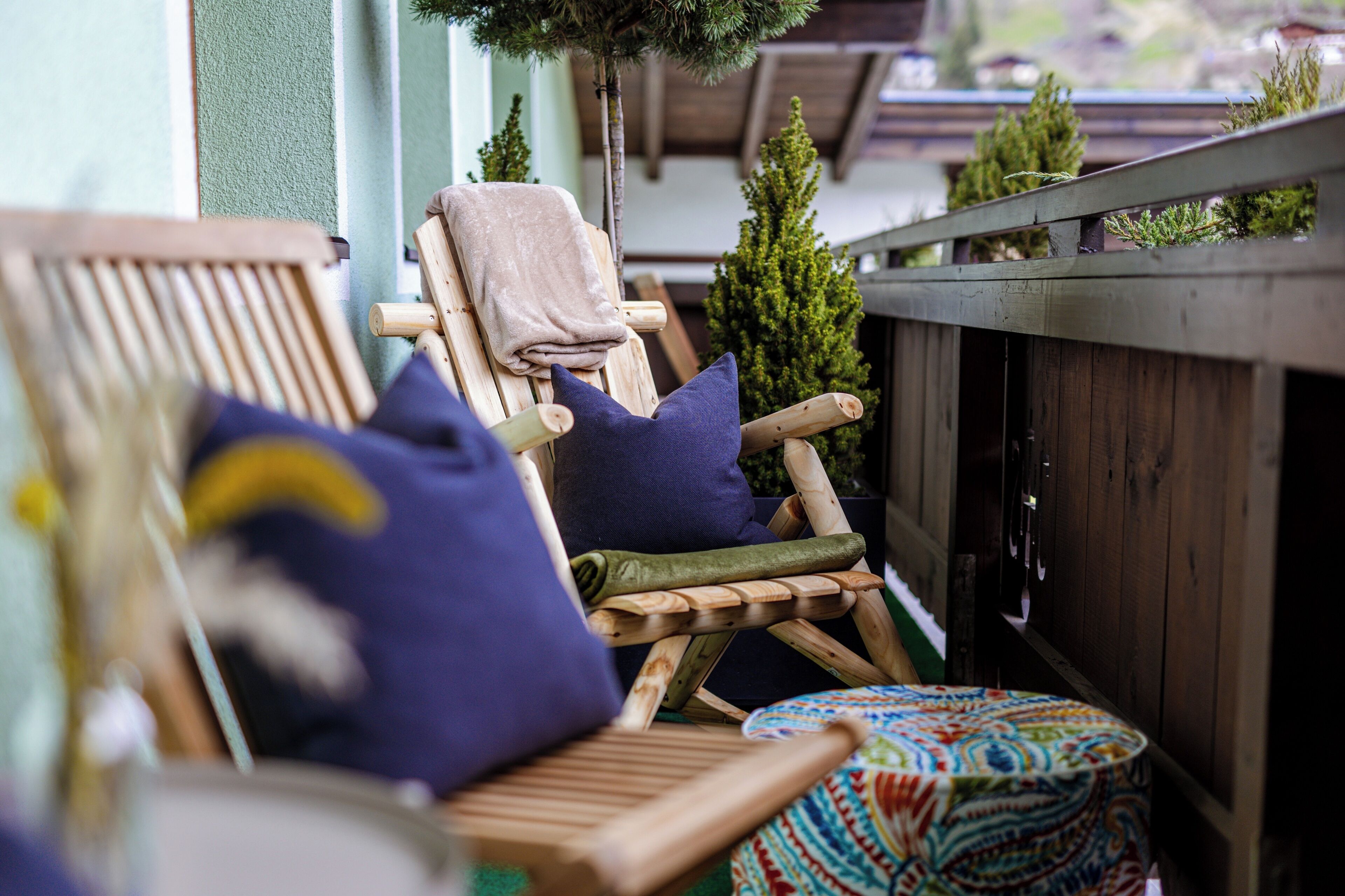 A wooden deck with a chair and a small table, surrounded by greenery and a wooden fence.