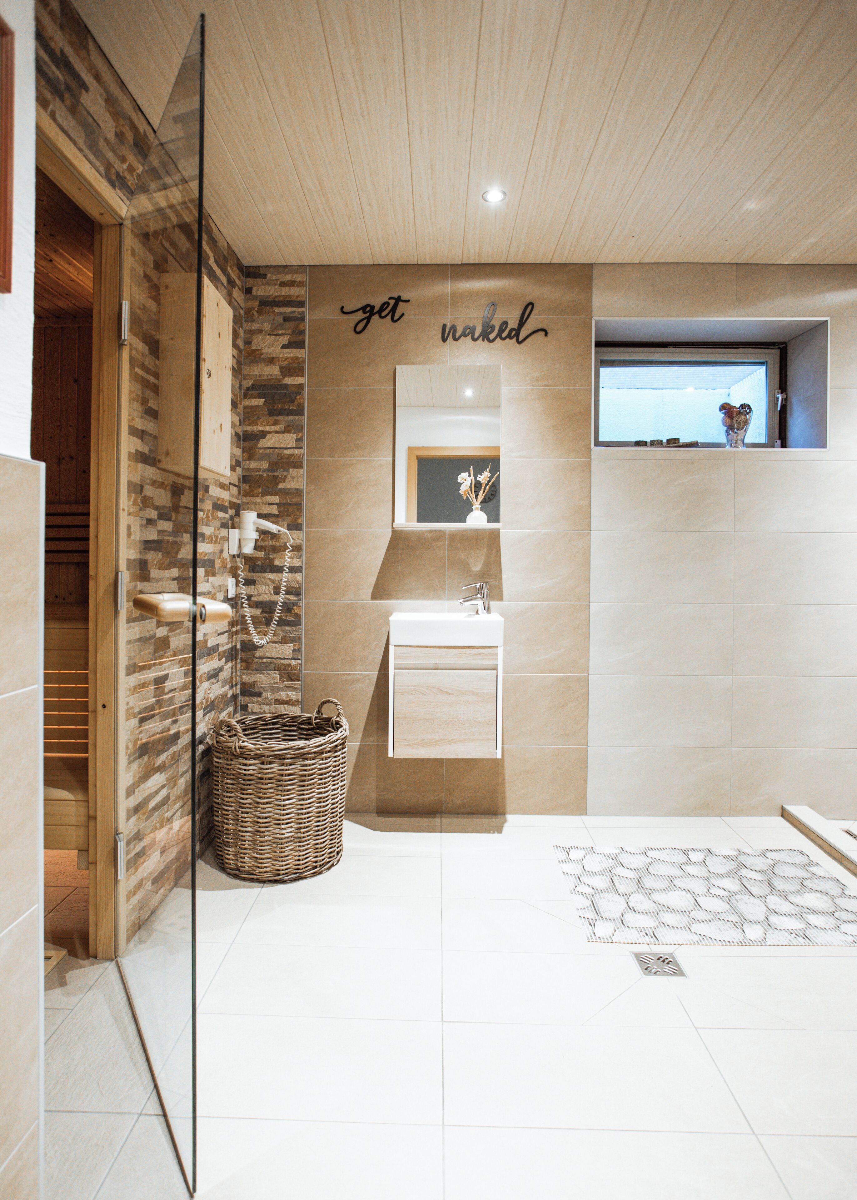 A modern bathroom with a wooden ceiling, a stone wall, a white sink, and a mirror.