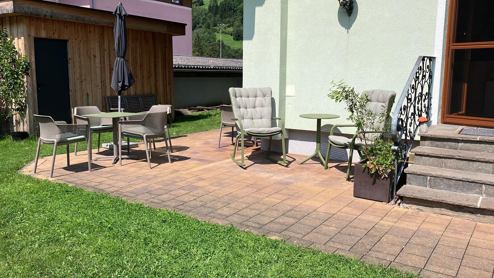 Un espace extérieur aménagé en patio, comprenant un coin salon avec des chaises et une table, une petite table ronde, et un escalier menant à l’entrée du bâtiment.