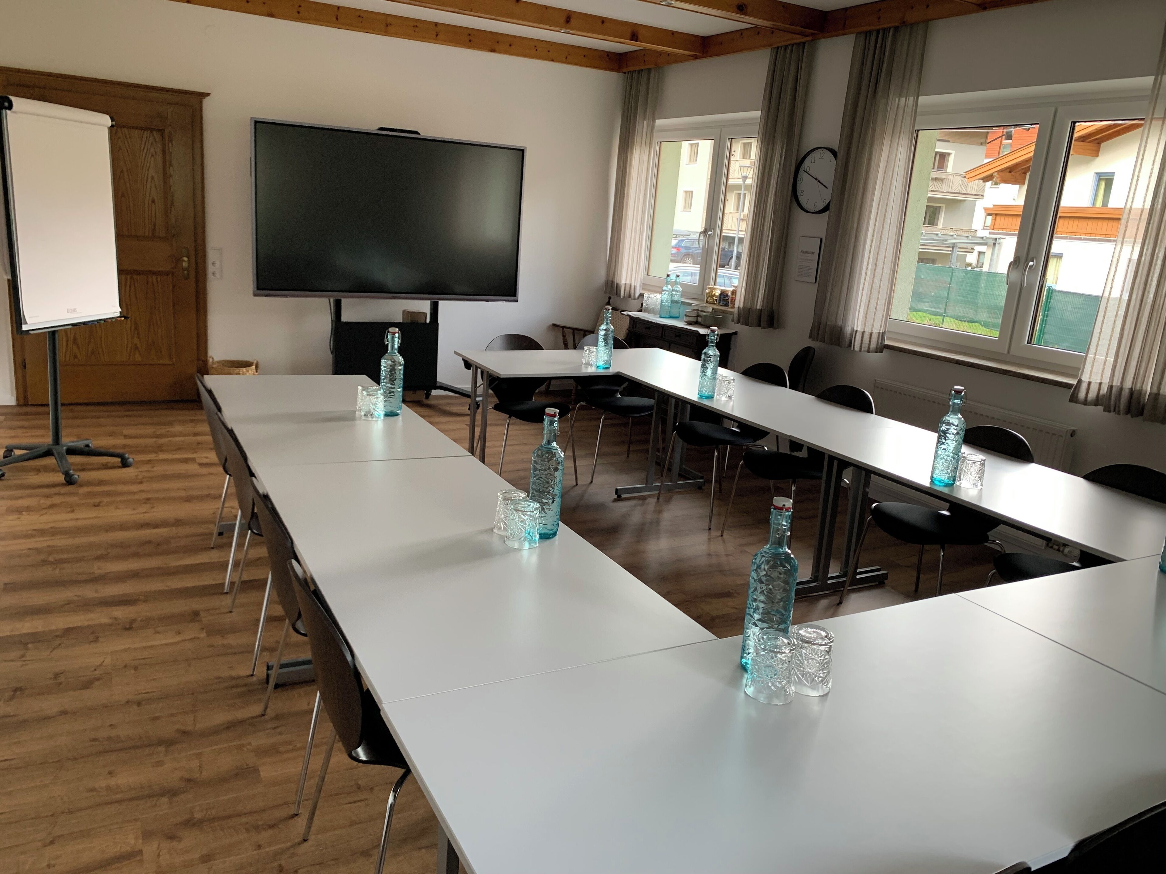Ein Konferenzraum mit langem Tisch, Stühlen, einer Projektionsleinwand und einer Uhr an der Wand.