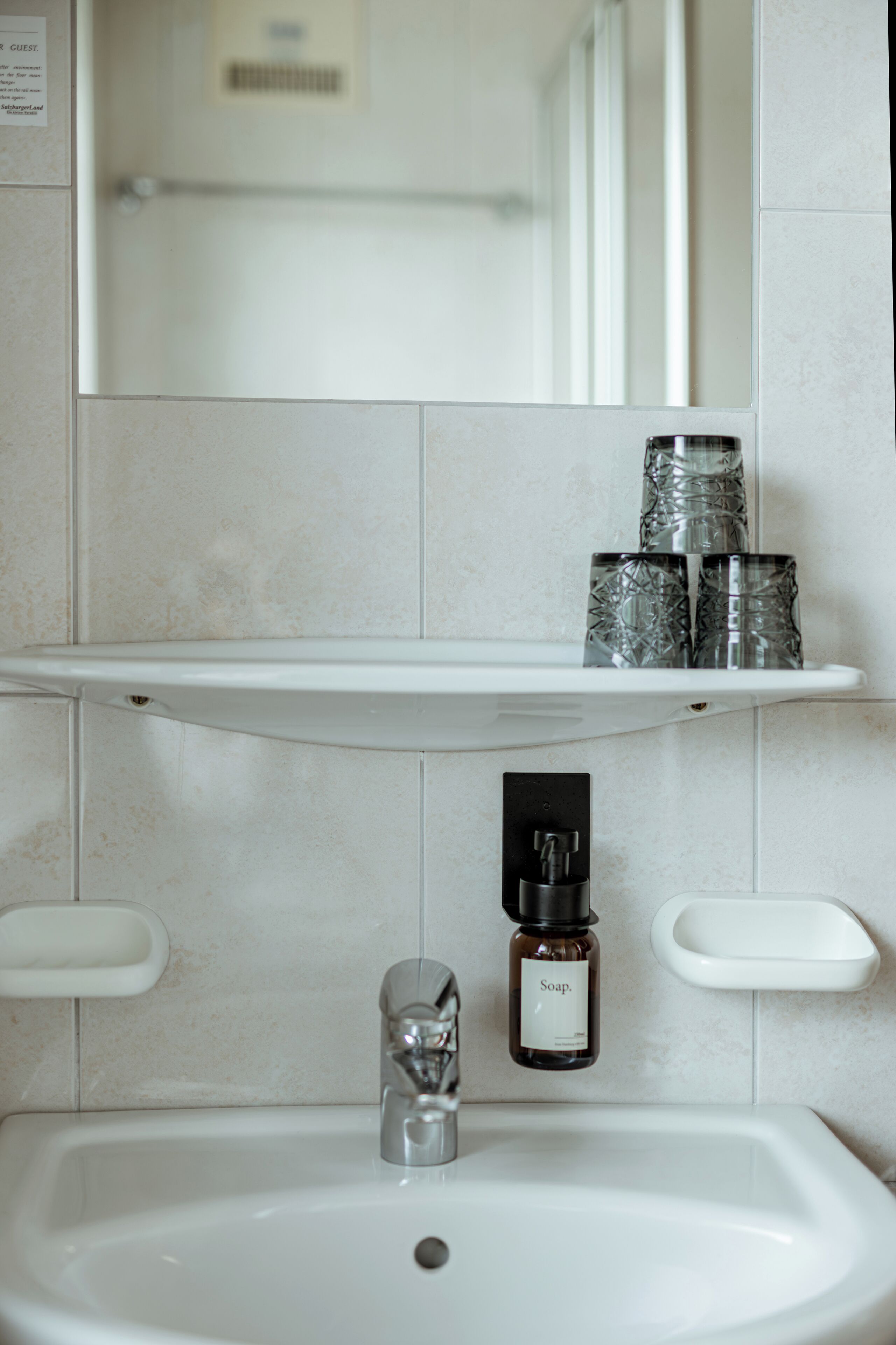 A bathroom with a white sink, a mirror above it, and a shelf with three glass containers.