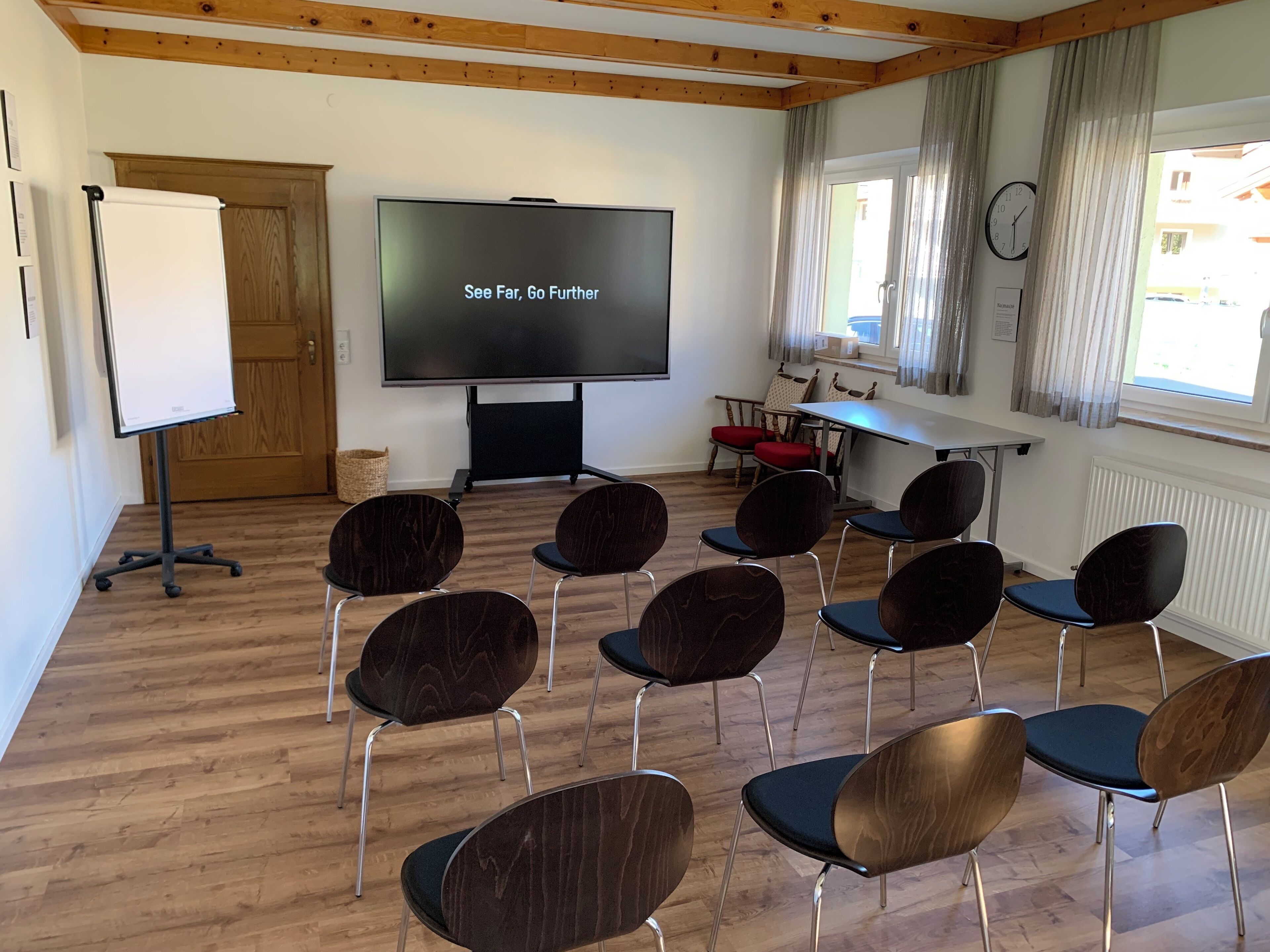 A conference room with a large screen displaying "See Far, Go Further," wooden floors, and modern chairs arranged around a table.