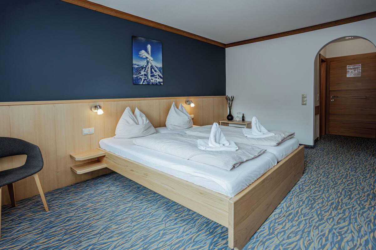 Una habitación de hotel con una cama de madera, un banco, una mesita de noche y un cuadro en la pared.