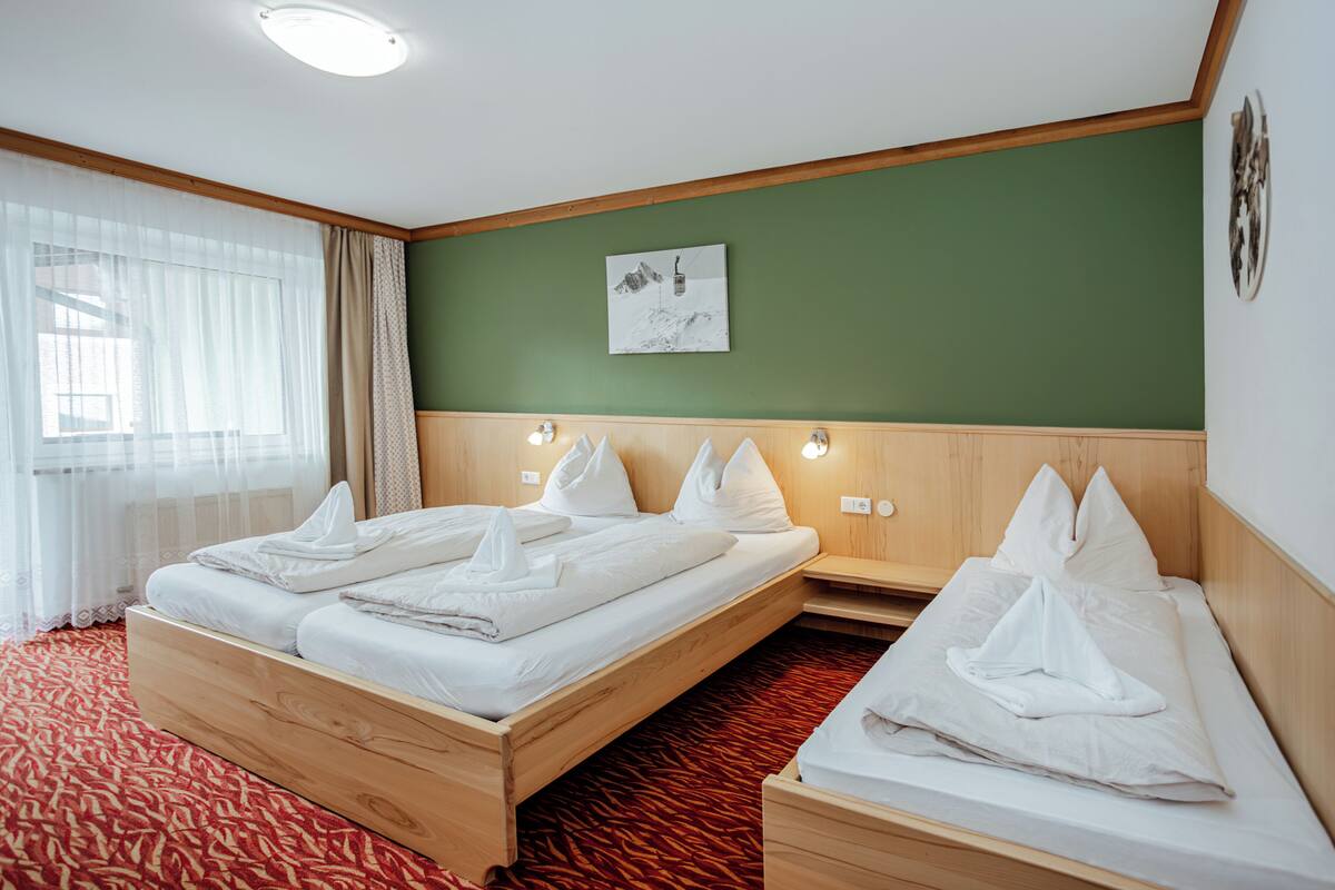Habitación de hotel con dos camas, una pared verde y un cabecero de madera.