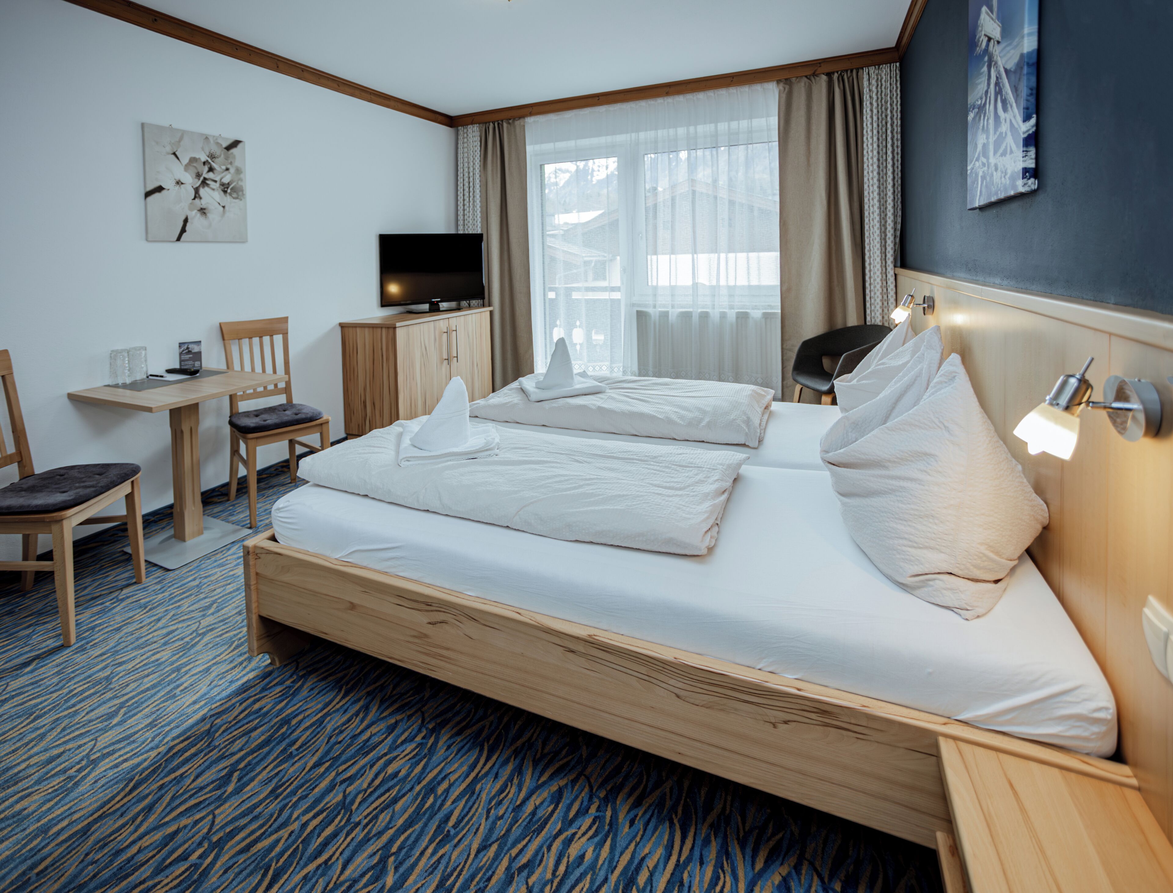 A hotel room with a large bed, a desk with a chair, a television, and a window with curtains.