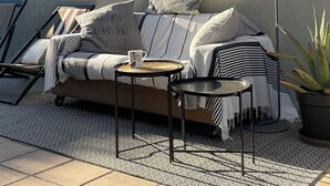En solig uteplats med sittmöbler, en soffa, fåtöljer, ett litet bord och en golvlampa.