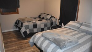 A bedroom with two beds, a wooden floor, a window with blinds, and a door.