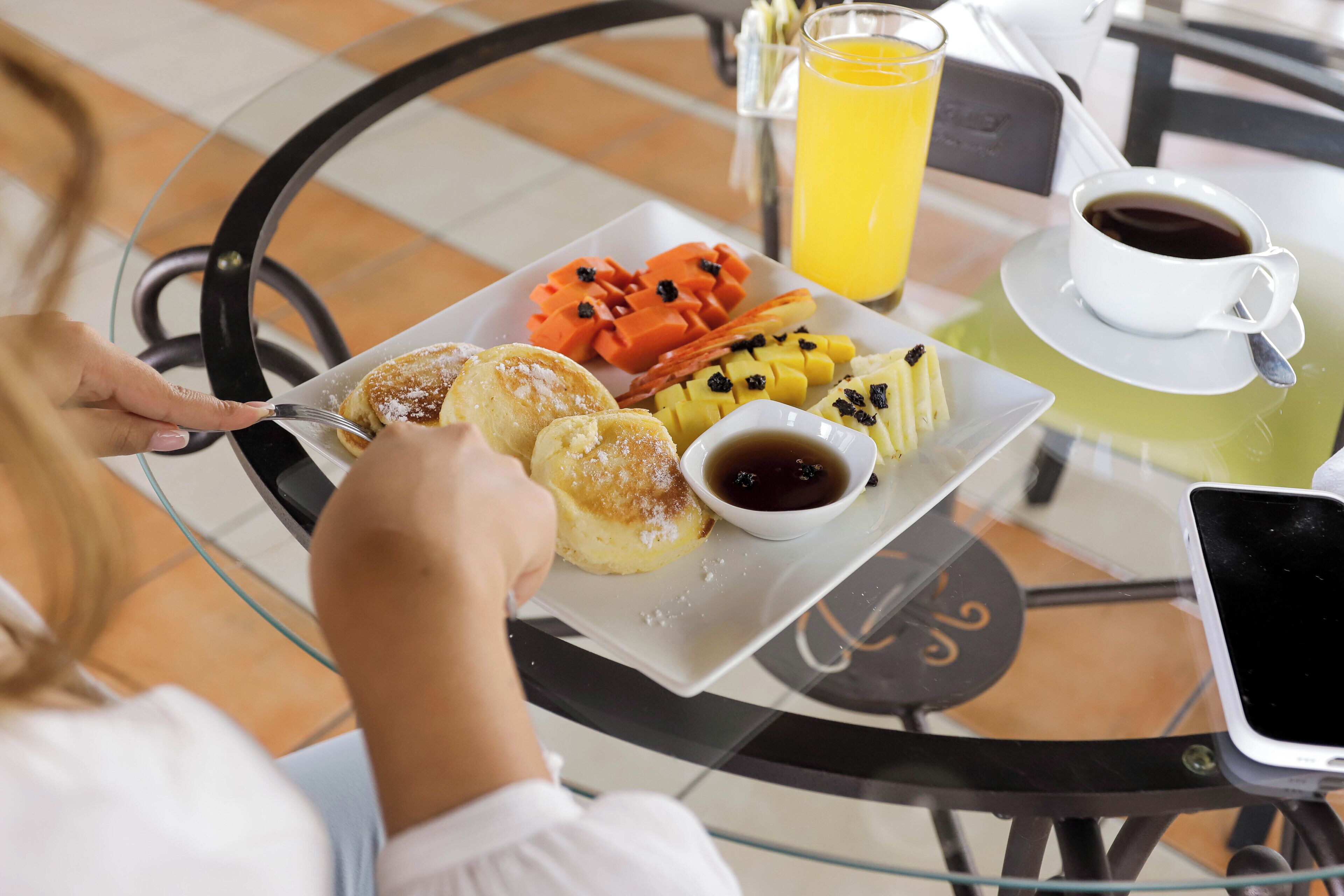 A breakfast setting with a plate of pastries, fruit, and a cup of coffee on a glass table.