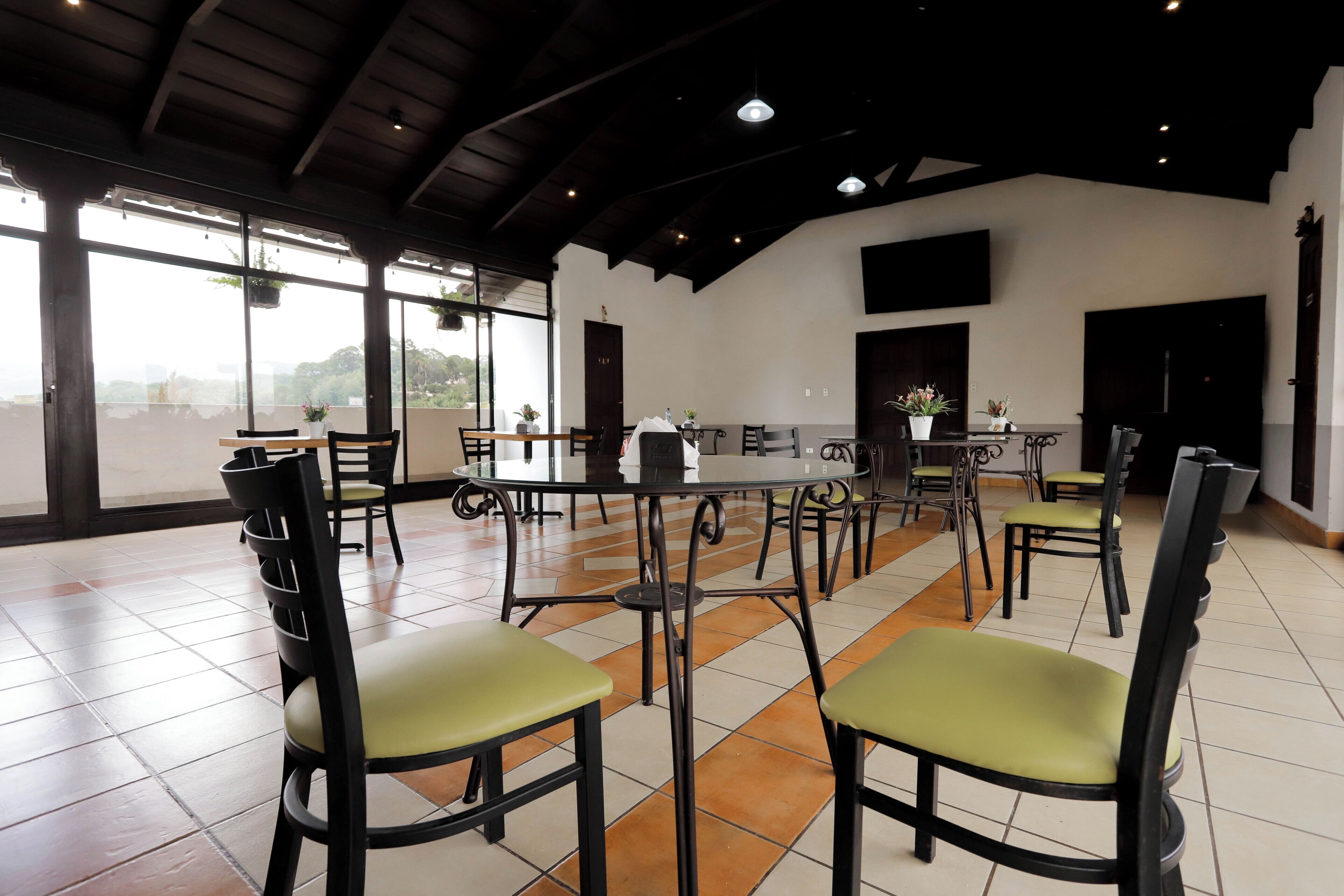 A spacious dining area with high ceilings and large windows, featuring multiple tables and chairs.