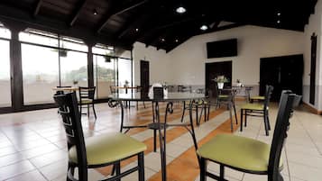 A spacious dining area with high ceilings and large windows, featuring multiple tables and chairs.