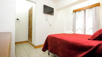 Ein Schlafzimmer mit Bett, Wandfernseher, Tür und einem mit Vorhängen versehenen Fenster.