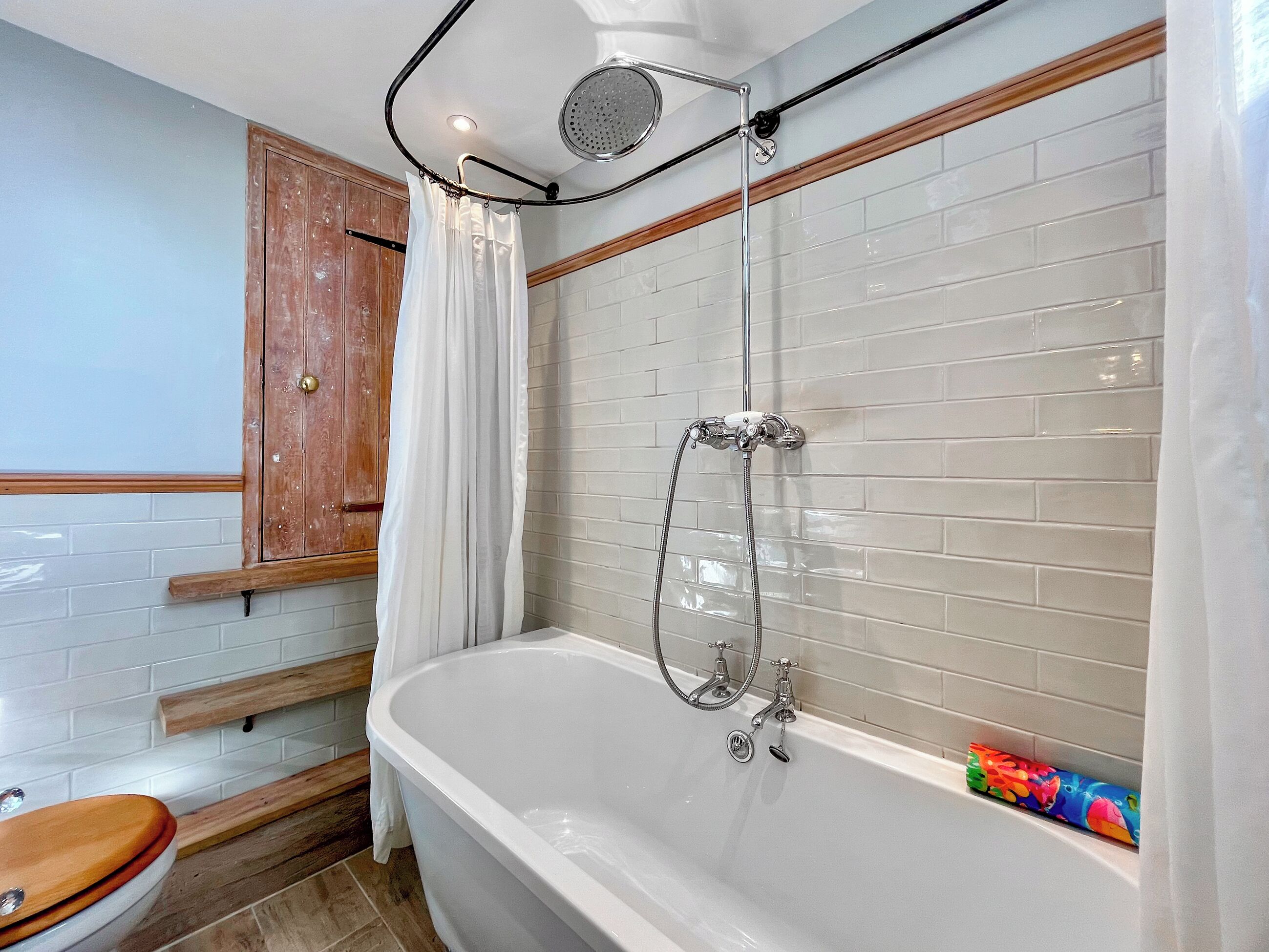 Een badkamer met een bad, douche, houten kast en witte betegelde wanden.