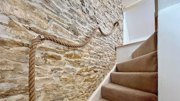 A stone wall with a rope, a carpeted staircase, and a white door.