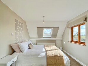 Quarto com cama, mesa de cabeceira, janela e claraboia.