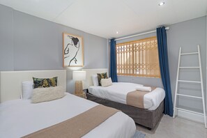 A hotel room with two beds, a ladder, a window with curtains, a wall-mounted artwork, and a bedside lamp. - Beachfront Bliss with Pool & Ocean Views (Cape Town)