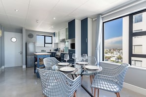 A modern kitchen with a dining area, large windows, and a view of the city. - Beachfront Bliss with Pool & Ocean Views (Cape Town)