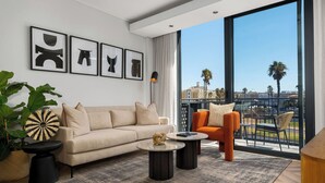 Een moderne woonkamer met een bank, twee bijzettafels en een groot raam met uitzicht op palmbomen en gebouwen.