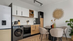 Een moderne keuken met een ingebouwde wasmachine en droger, houten kastjes en een eethoek met een ronde tafel en stoelen.