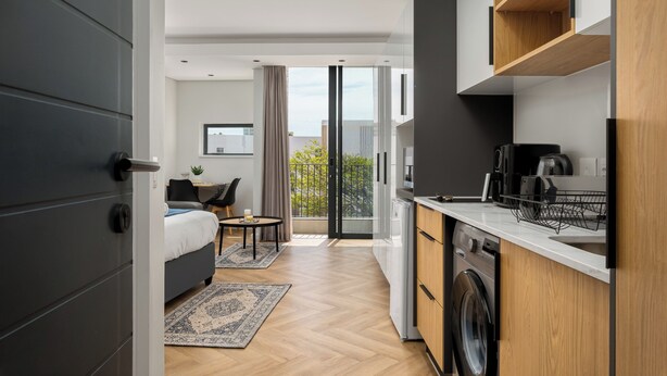 A modern hotel room with a balcony, a compact kitchen, and a neatly arranged bed. - On Park | Modern Century City Studio (Cape Town)